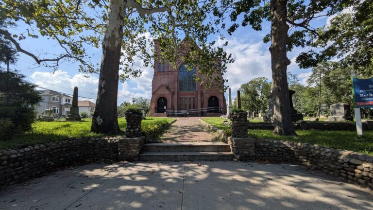 Brick church behind a low stone wall and mature trees in Tottenville