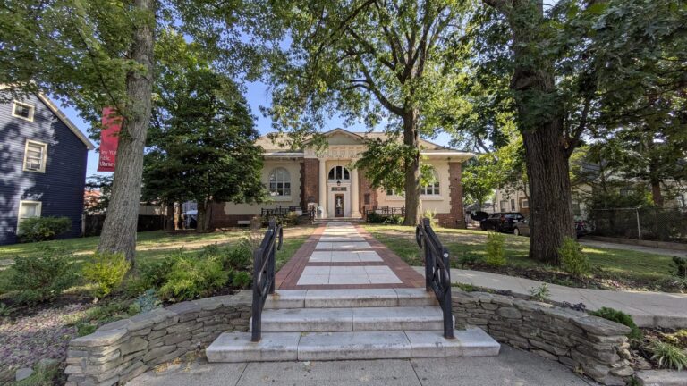 Brick civic building at the top of a wide paved walk with iron railings in Tottenville