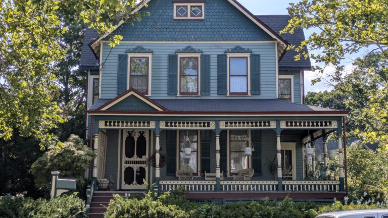 Blue Victorian house with a wraparound porch and carved trim in Tottenville