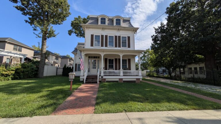 White house with a mansard roof and a brick path to the front porch in Tottenville