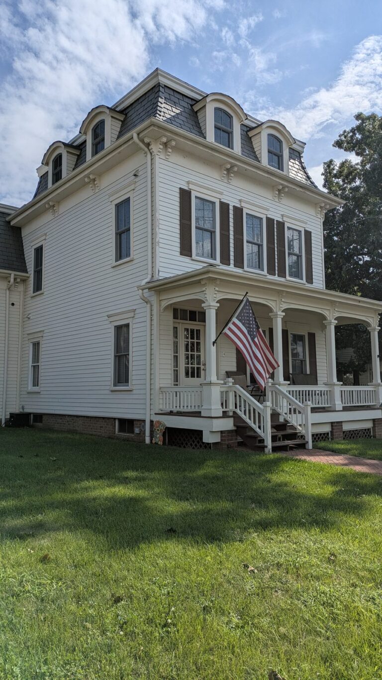 White Second Empire house with dormer windows and a flag on the porch in Tottenville