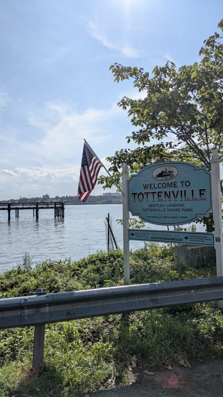 Welcome to Tottenville sign beside a flag with Raritan Bay in the background