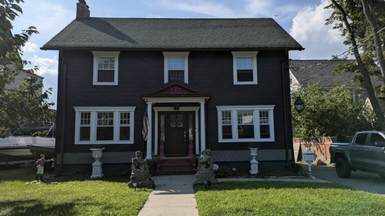Dark shingled colonial house with white window trim and a pedimented entrance