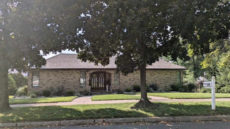 Single storey brick house behind a large shade tree in Tottenville