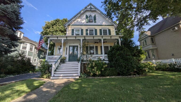 Pale green Victorian house with a white covered porch and a flag by the steps