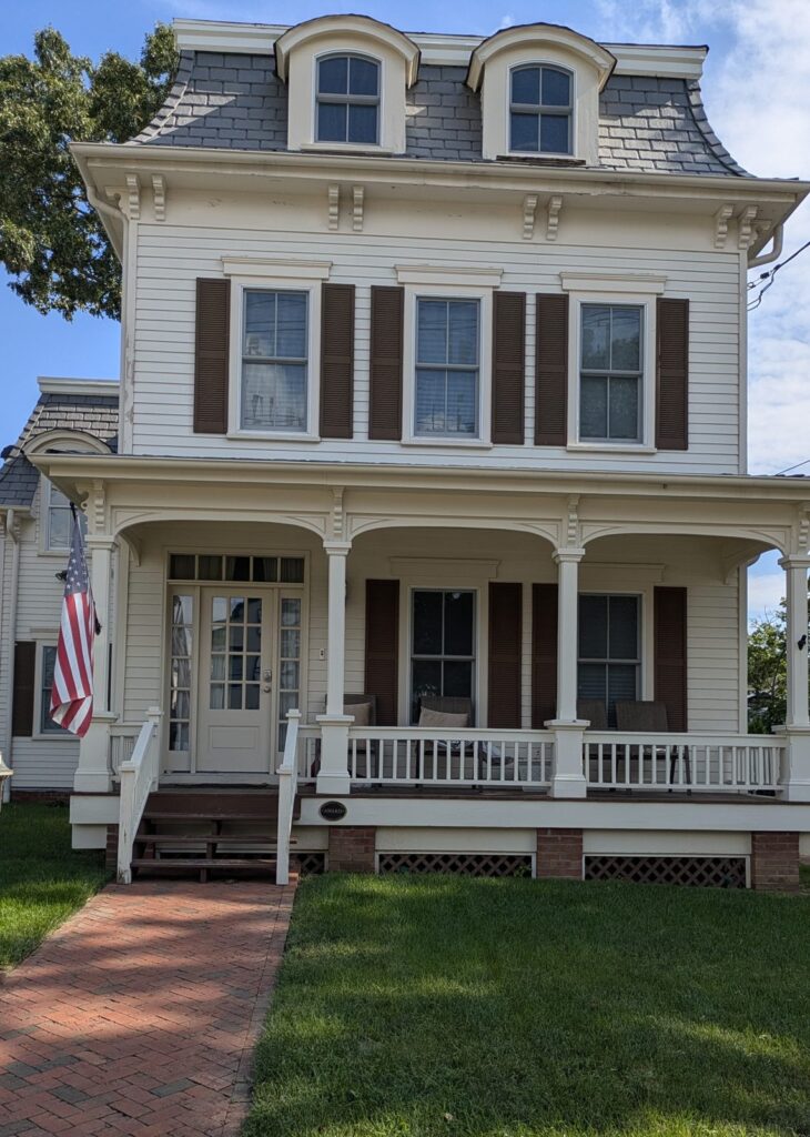 A cream Second Empire house with a mansard roof and a front porch on a Tottenville street